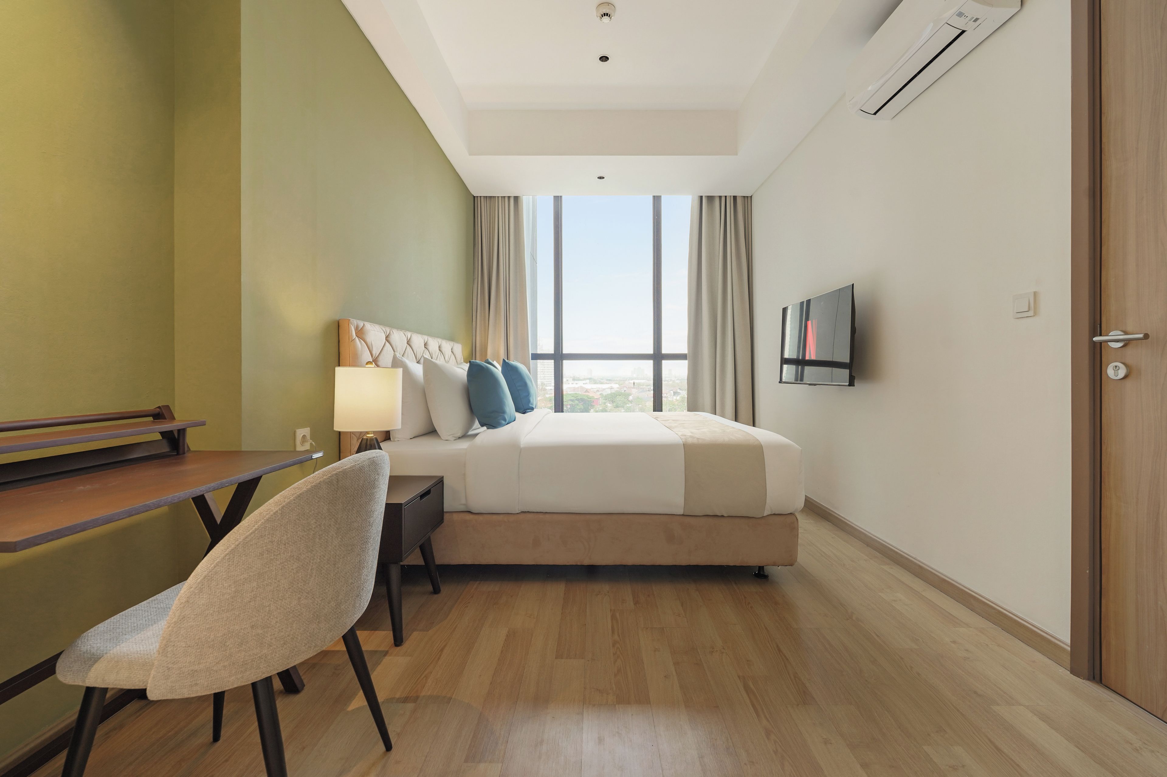 Ein Hotelzimmer mit Bett, Schreibtisch, Stuhl, Fernseher und einem Fenster mit Blick auf die Stadt.