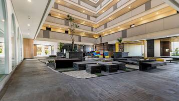 A spacious atrium with a modern design, featuring a central open area with seating and planters, and a multi-level ceiling with recessed lighting.