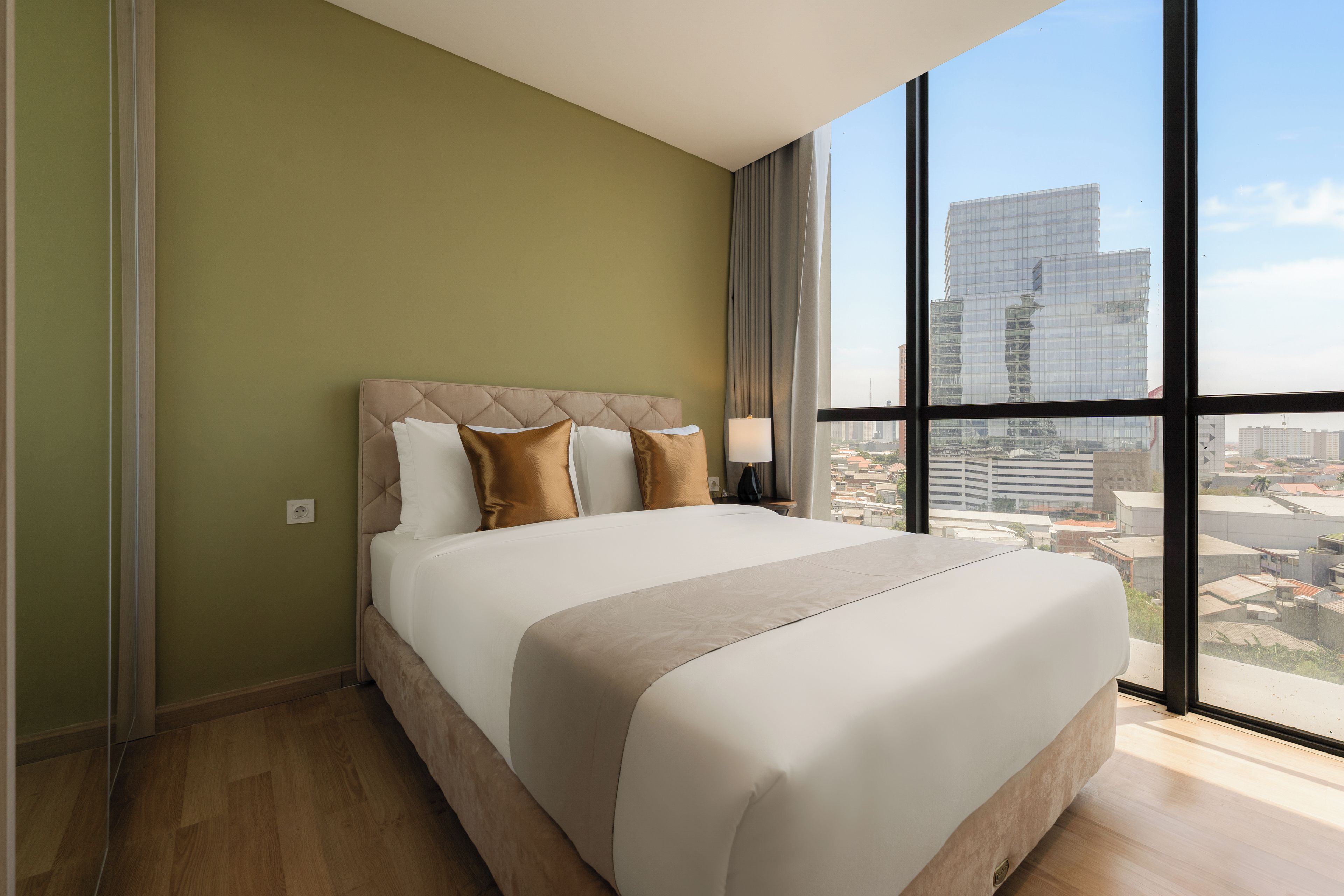 A hotel room with a large bed, a view of the city through floor-to-ceiling windows, and a green wall.