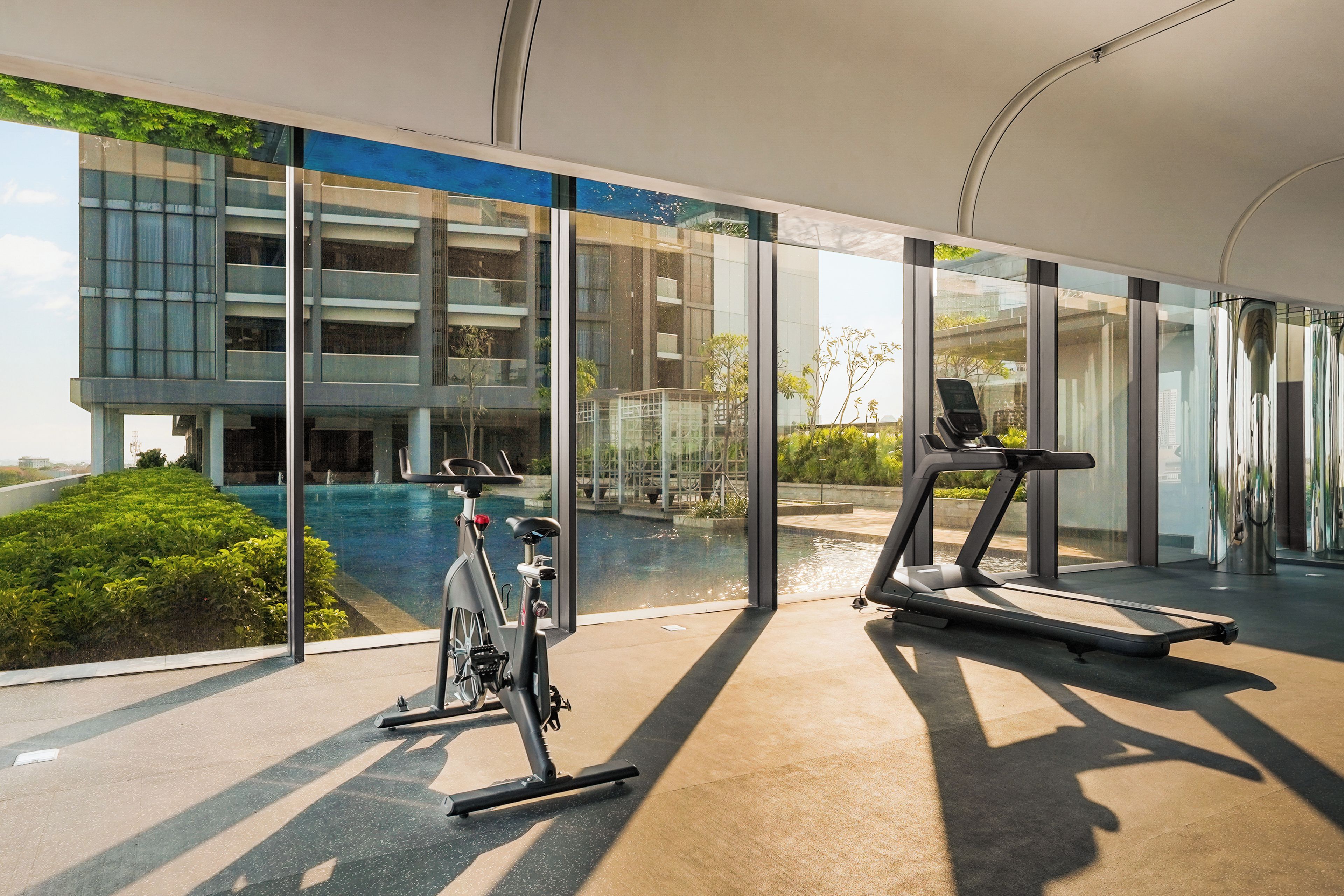 Un gimnasio moderno con equipo de ejercicio, una ventana grande con vistas a una piscina y un edificio.