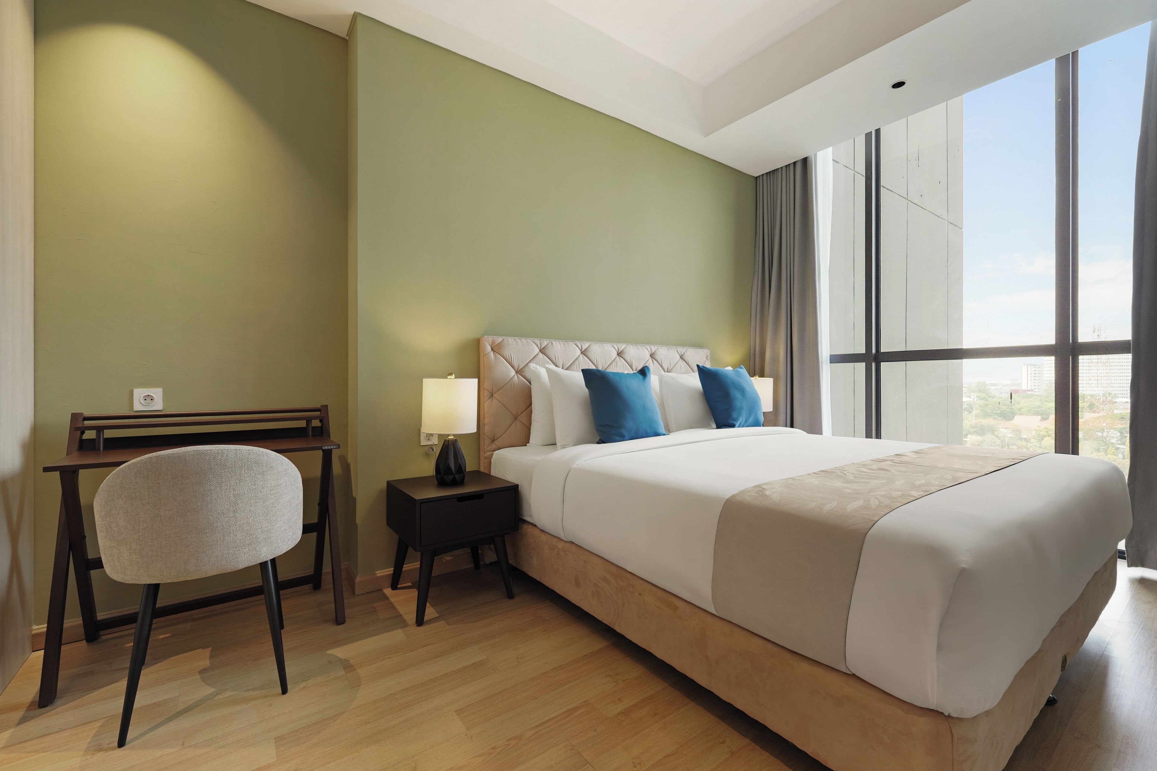 A hotel room with a large bed, a desk, a chair, and a window with a city view.