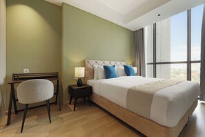 A hotel room with a large bed, a desk, a chair, and a window with a city view.
