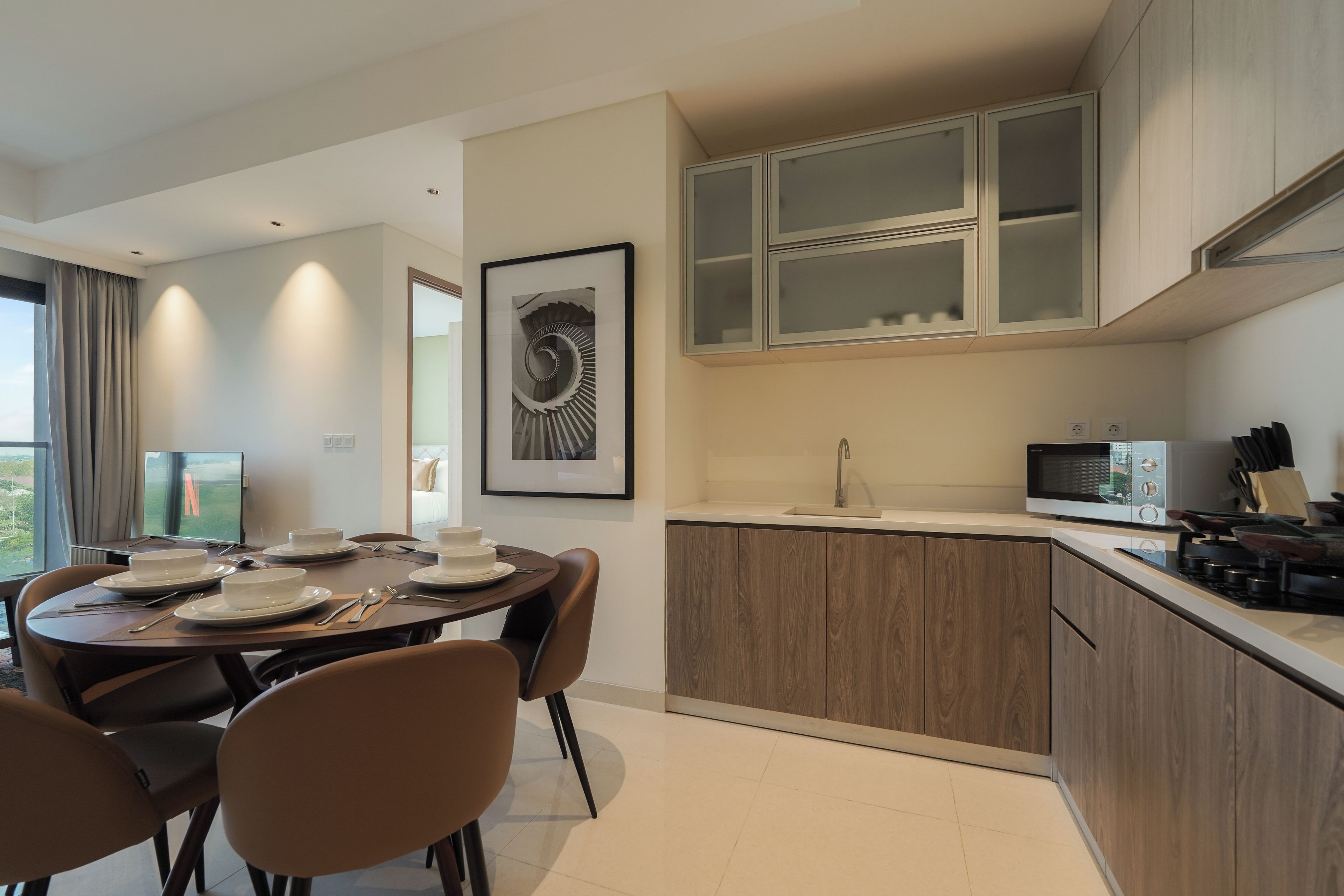 A modern kitchen with a dining area, featuring a round table with chairs, a built-in oven, and a microwave.
