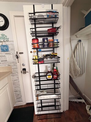 Eine Tür mit einem schwarzen Metallorganisator, der verschiedene Küchenutensilien wie Gewürze, Soßen und eine Flasche Barbecue-Sauce enthält.
