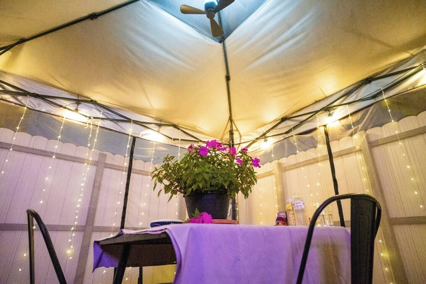 Une tente équipée d’une table et de chaises, d’un ventilateur de plafond et de guirlandes lumineuses.