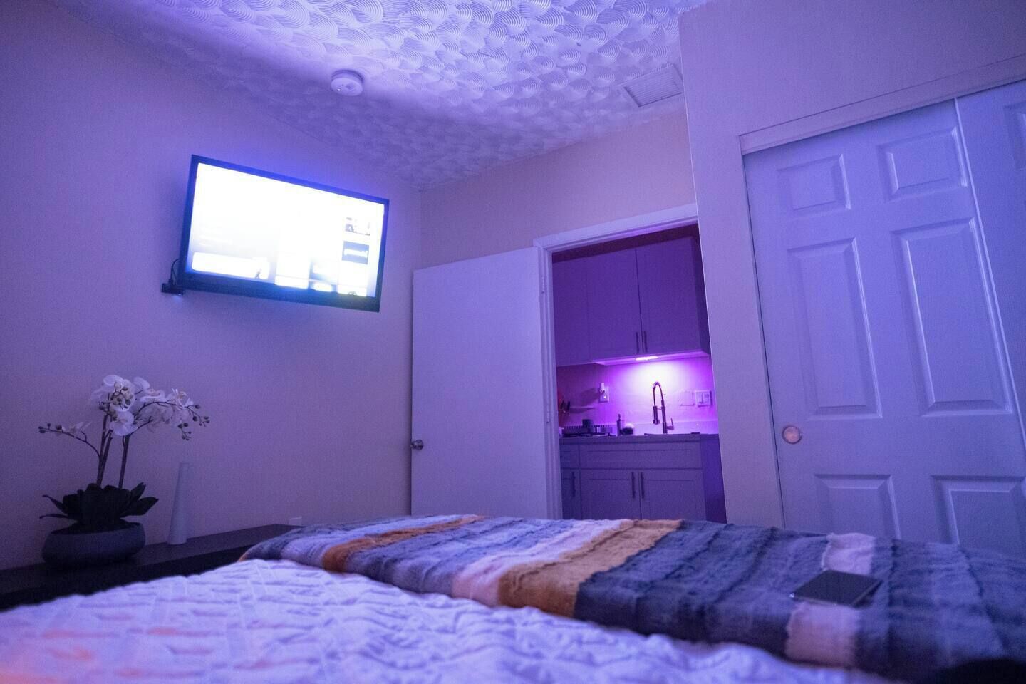 Quarto com cama, televisão na parede e vista para a cozinha.
