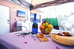 A table with a bottle of wine, a bowl of fruit, cheese, and crackers, set on a tablecloth with a tent overhead. - BayNest Cozy South Miami Suite Long Stay Friendly (Cutler Bay)