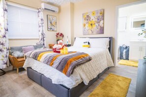 Une chambre à coucher avec un lit, une chaise, une fenêtre avec des rideaux et un tableau accroché au mur.
