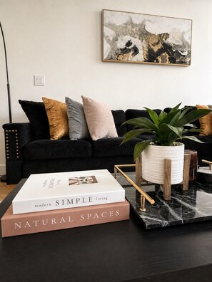 Un salon moderne avec un canapé noir, une table basse sur laquelle repose un livre intitulé « ESPACES NATURELS », et une plante en pot.