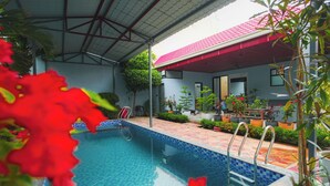 Una piscina con borde de baldosas, rodeada de plantas en macetas y una zona de patio techada.
