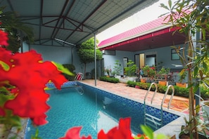 A swimming pool with a tiled edge, surrounded by potted plants and a covered patio area. - Panther Farm Patrakar (Jaipur)