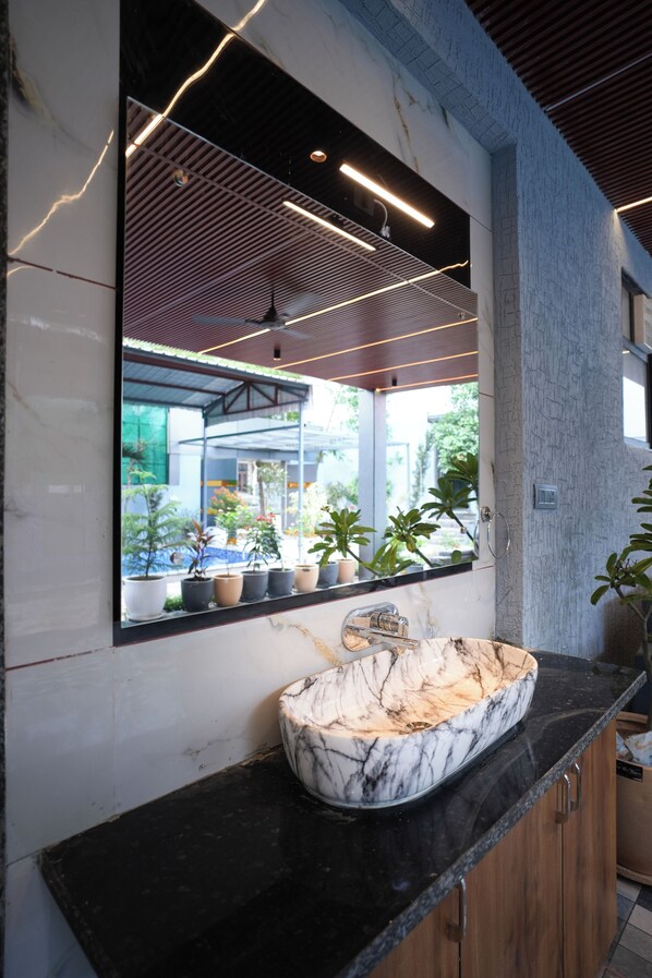 A modern bathroom with a marble sink, a large mirror, and potted plants.