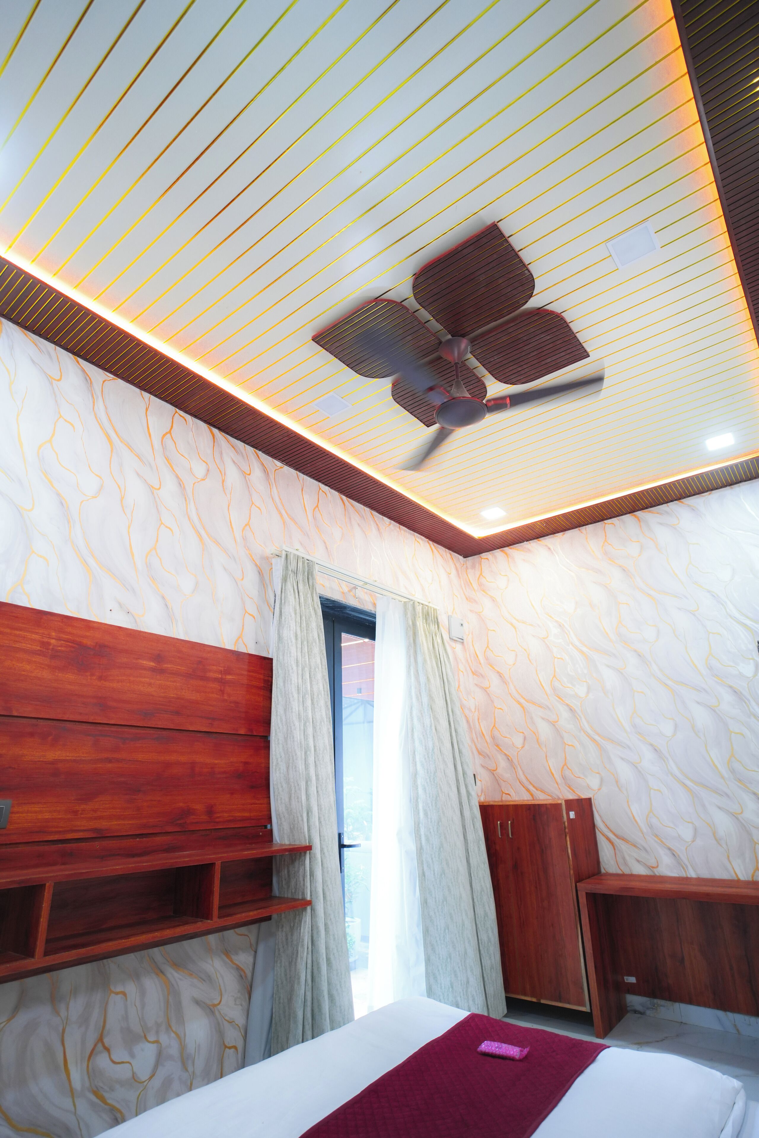 Ein Schlafzimmer mit einem Bett, einem Holzkopfende, einem Deckenventilator und einem Fenster mit Vorhängen.