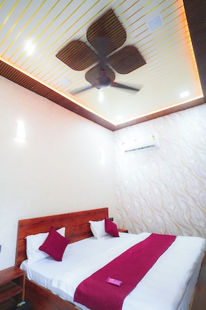 A hotel room with a bed, wooden headboard, white bedding, a ceiling fan, and a patterned wall.