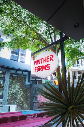 A sign for 'Panther Farms' hanging from a structure with a view of buildings and trees in the background.