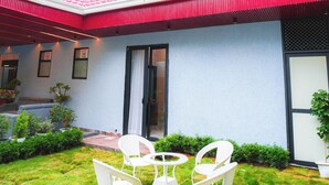 Un patio con sillas blancas y una mesa, un techo rojo y una pared blanca con una puerta.
