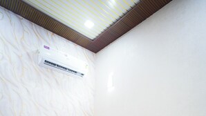 Habitación de hotel con una cama grande, ropa de cama blanca, una manta roja y un equipo de aire acondicionado en la pared.