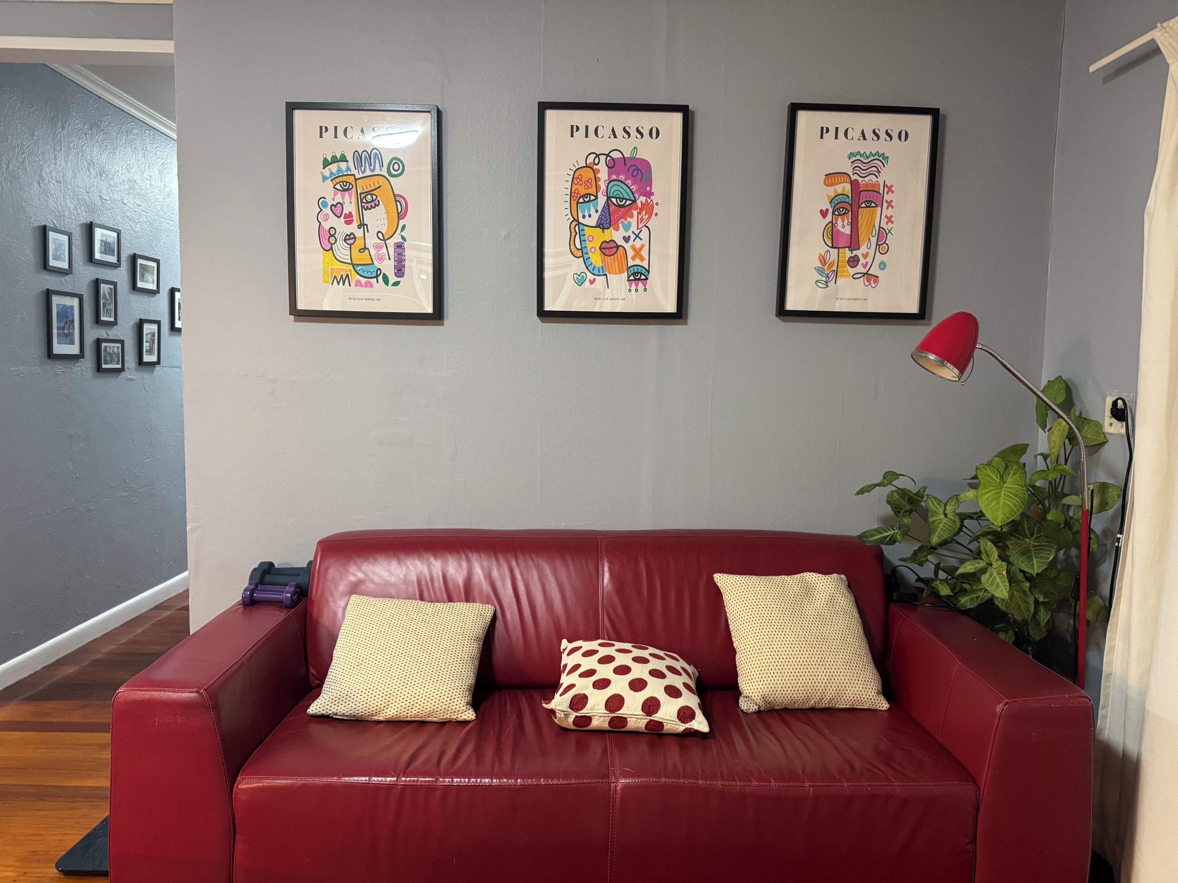 A red leather sofa with patterned cushions, a red floor lamp, and three framed artworks on the wall.