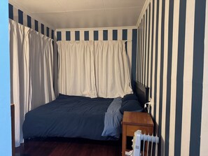 Ein Schlafzimmer mit Bett, Vorhängen, einem Nachttisch und einem Heizkörper.