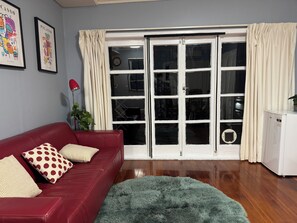 Ein Wohnzimmer mit einem roten Sofa, einem grünen Fellteppich, einem weißen Schrank und einer Glastür mit Vorhängen.