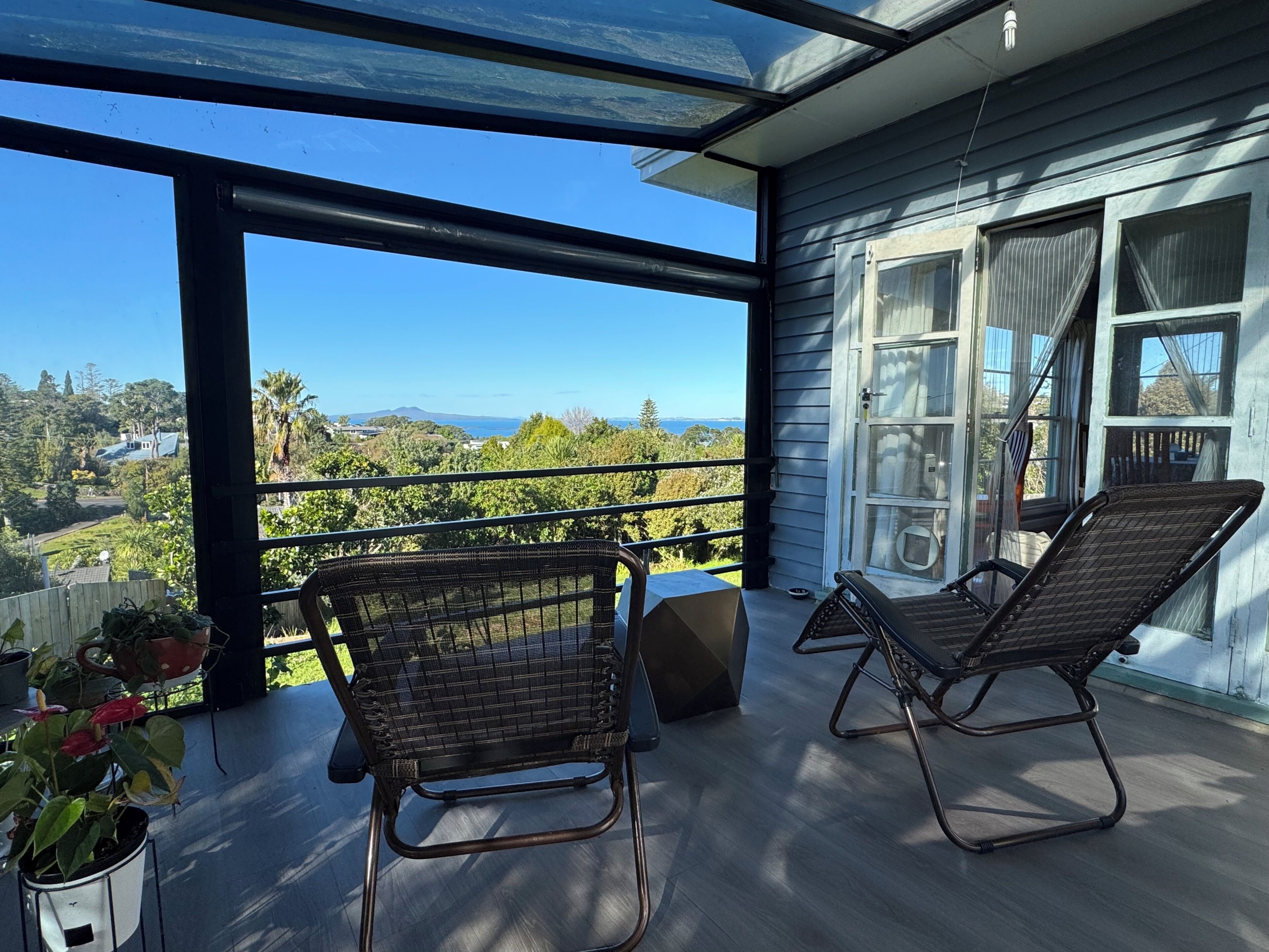 Ein Balkon mit zwei Korbstühlen, einem Blumentopf und Blick auf eine Hügelkette.