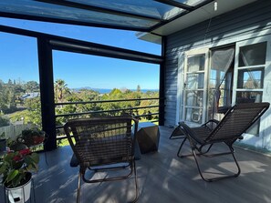 Ein Balkon mit zwei Korbstühlen, einem Blumentopf und Blick auf eine Hügelkette.