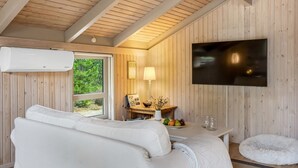 En modern inredning med en vit soffa, en platt-TV som är monterad på väggen och en matplats med ett bord och stolar.