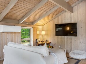 A modern interior with a white sofa, a flat-screen TV mounted on the wall, and a dining area with a table and chairs. - "Pia" - 685m from the sea by Interhome (Læsø)