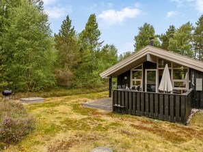 Una cabaña con terraza, mobiliario exterior y una parrilla.