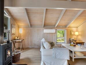 A cozy cabin interior with a wooden ceiling, a sofa, a table, a fireplace, and a window with a view of greenery. - "Pia" - 685m from the sea by Interhome (Læsø)