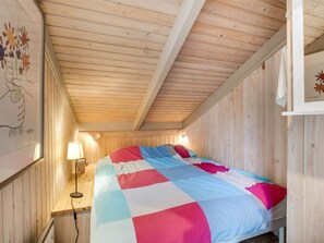 Habitación con paneles de madera, una cama, una mesita de noche, una lámpara y obras de arte en las paredes.