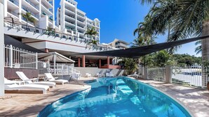 A swimming pool with lounge chairs and a building with balconies in the background. - Marina Views at Airlie 10H (Airlie Beach)