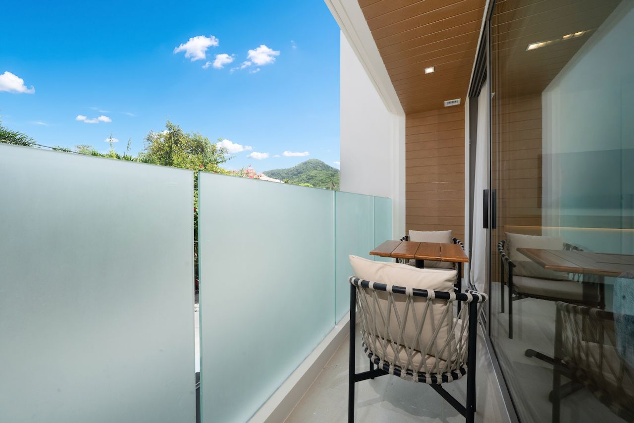 A balcony with a glass partition, a table, and a cushioned chair.