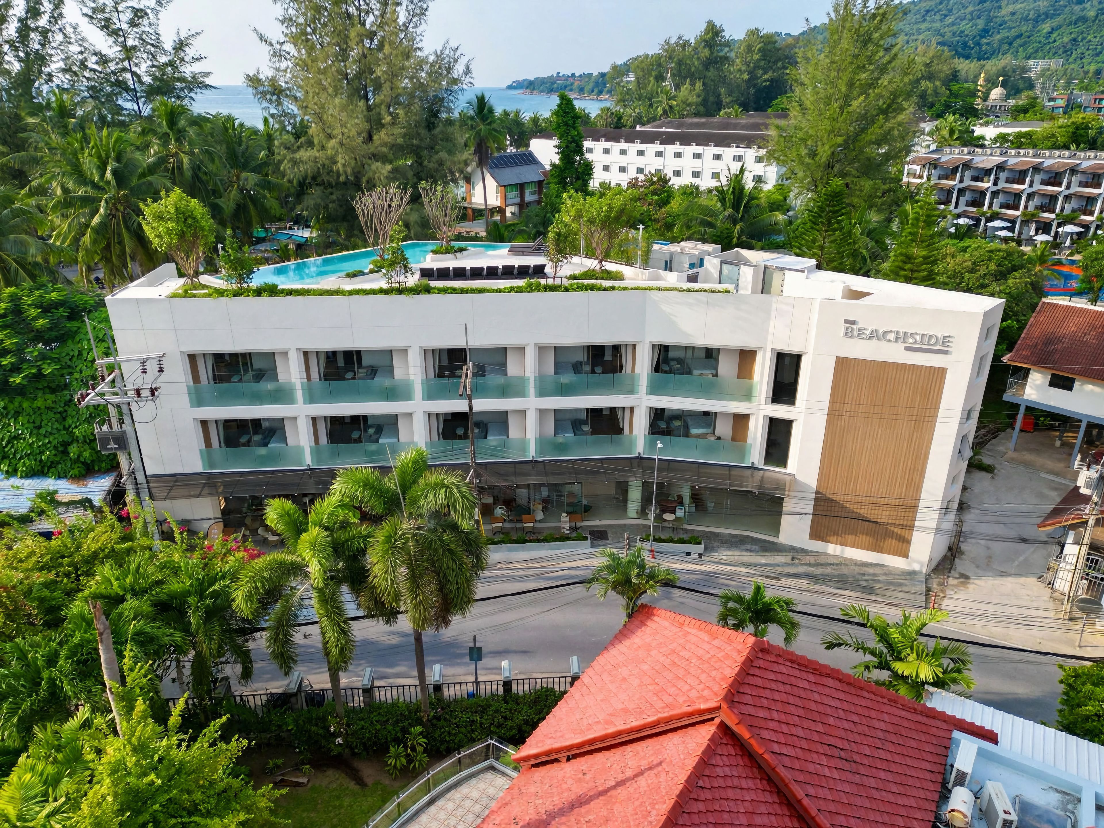 Un hotel con piscina en la azotea, varios balcones y vista al mar.