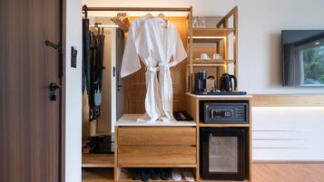 Quarto de hotel com guarda-roupa de madeira, minibar, máquina de café e televisão na parede.