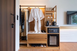 A hotel room with a wooden wardrobe, a minibar, a coffee machine, and a TV mounted on the wall. - The Beachside By Himmapana (Kamala)