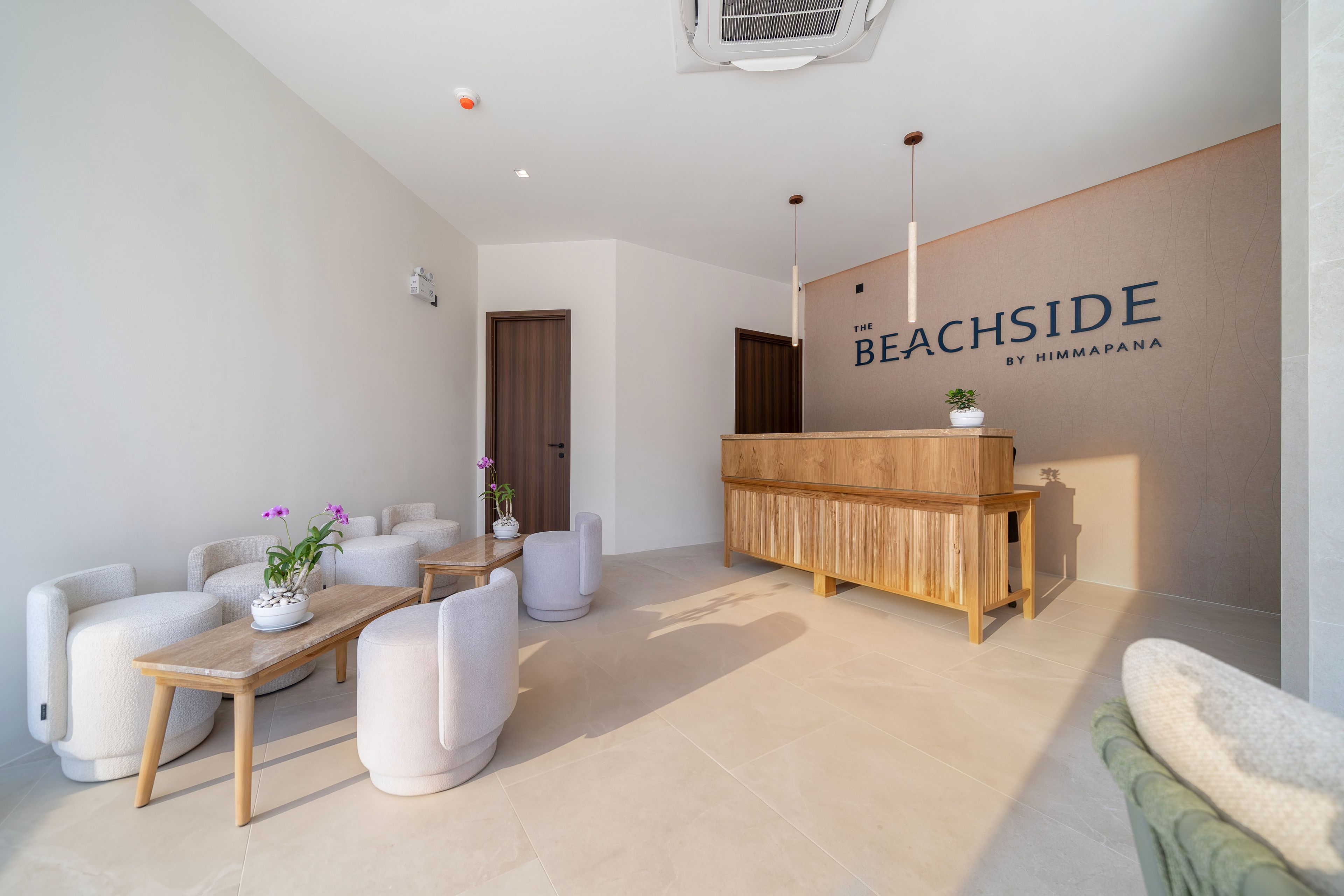 A reception area with a wooden reception desk, a seating area with cushioned chairs, and a wall with the text 'The Beachside by Himmapana'.