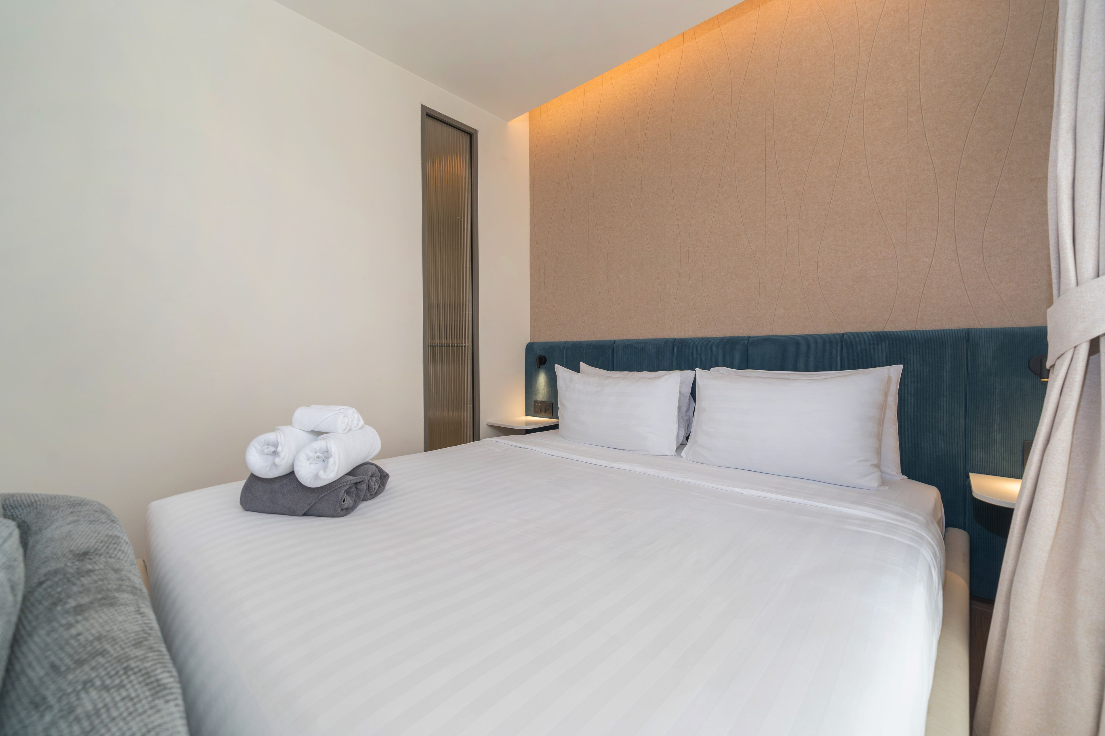 A hotel room with a neatly made bed, a side table with a lamp, and a chair.