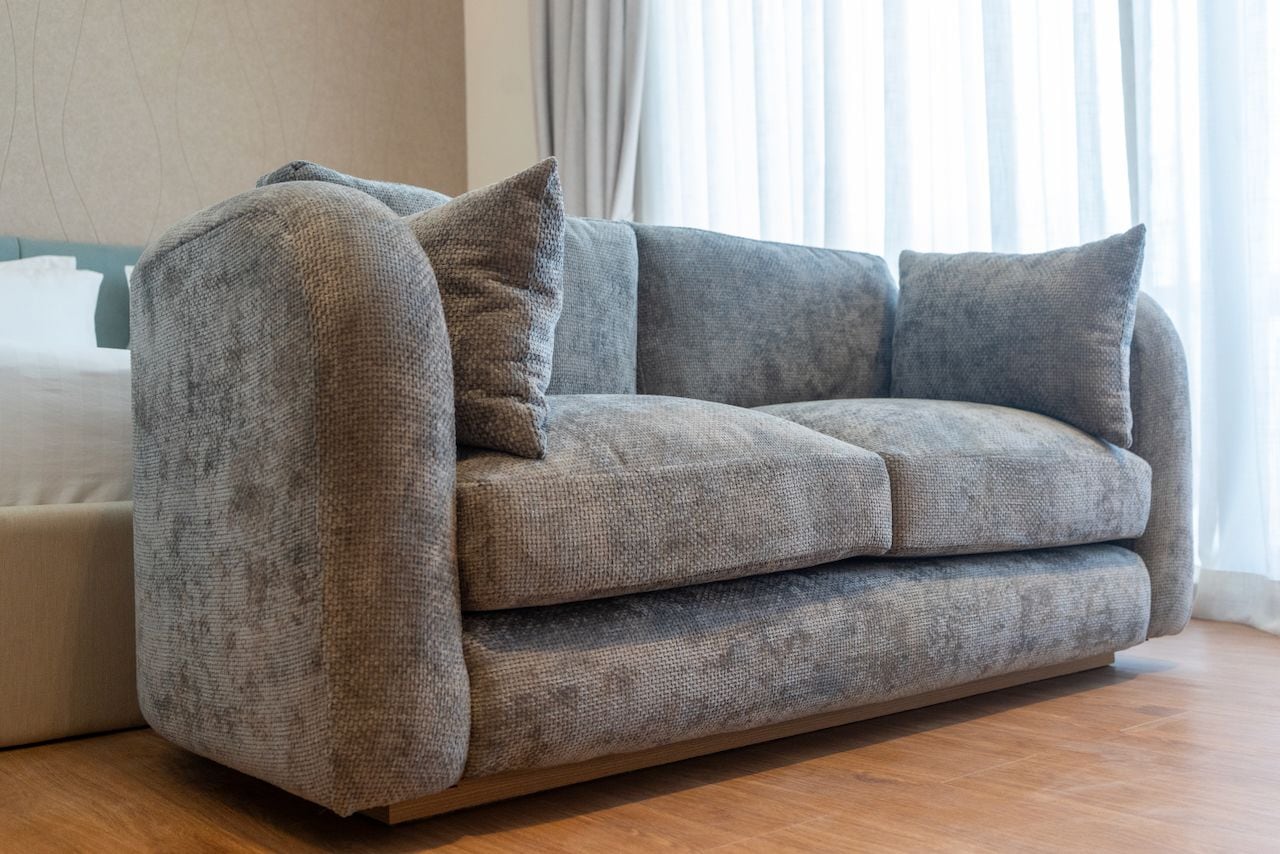 A grey sofa with a matching throw pillow in a room with wooden flooring.