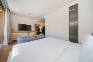 A modern hotel room with a large bed, a flat-screen TV mounted on the wall, a seating area with a sofa, and a wooden wardrobe. - The Beachside By Himmapana (Kamala)