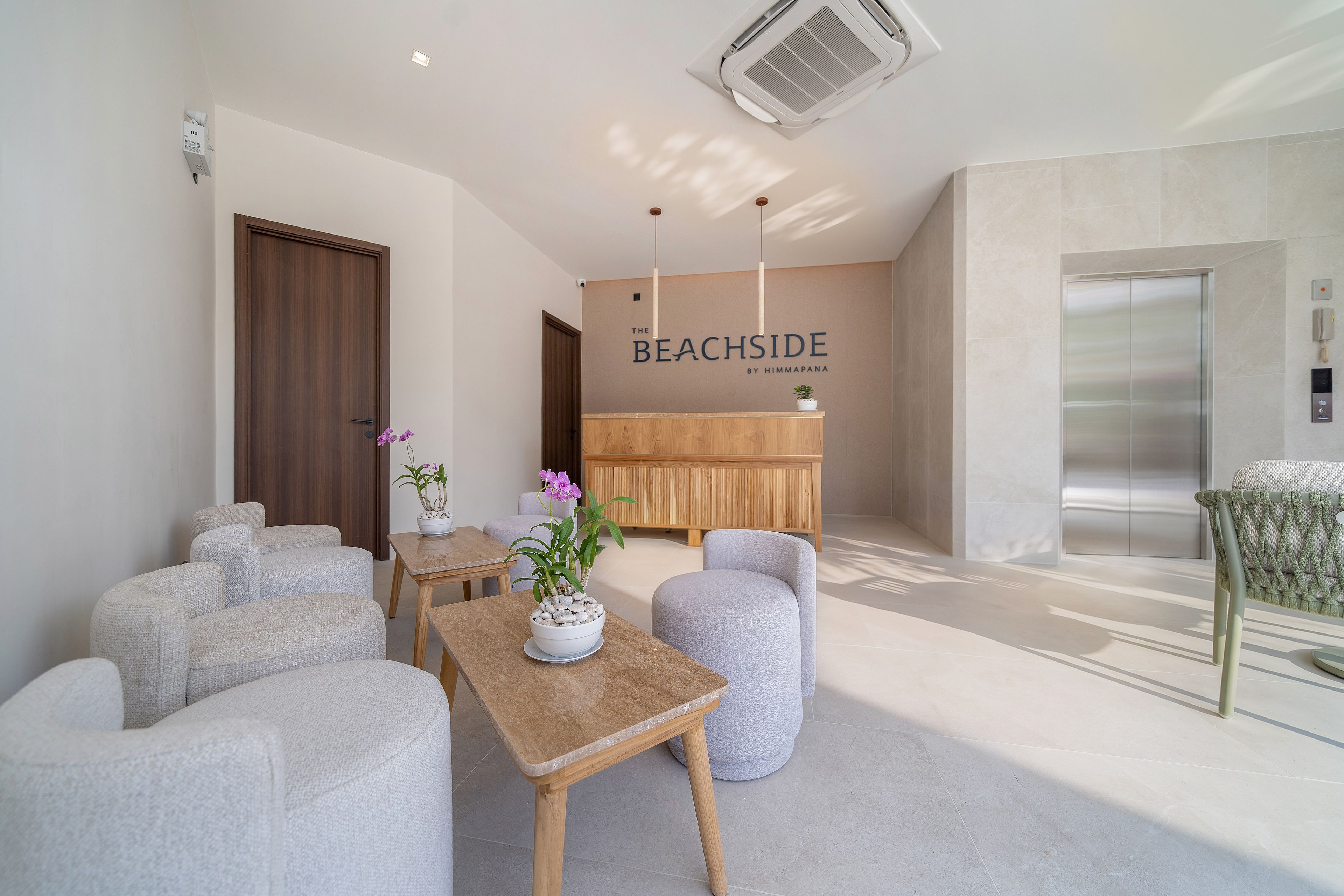 A modern hotel lobby with a reception desk, seating area, and an elevator.