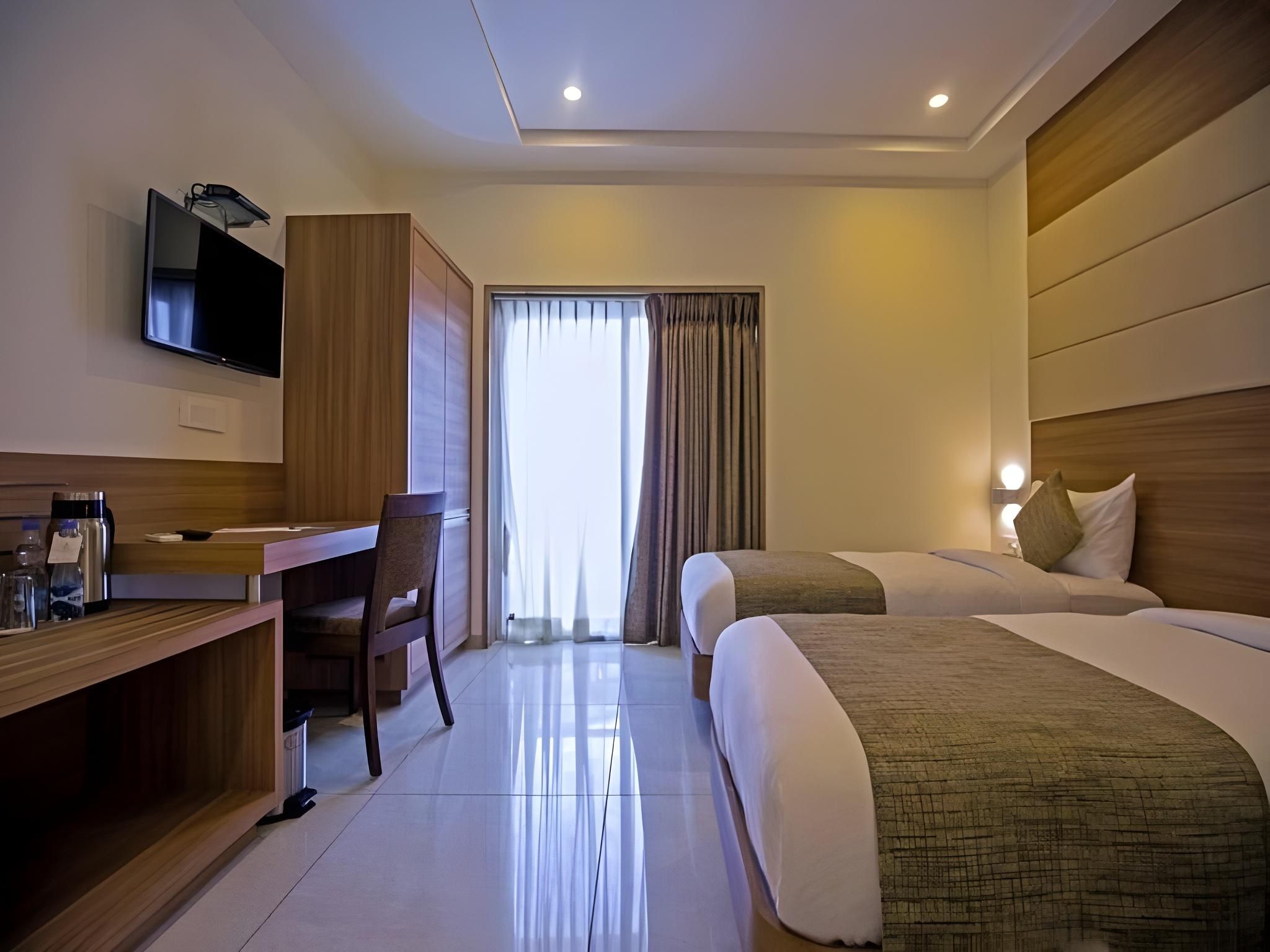 Habitación de hotel con escritorio, dos camas, televisor y ventana con cortinas.