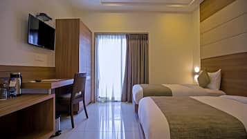 Habitación de hotel con escritorio, dos camas, televisor y ventana con cortinas.