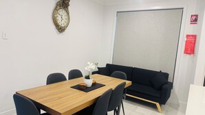 Een vergaderruimte met een houten tafel, zwarte stoelen, een witte orchidee, een decoratieve klok, een zwarte bank en een bord met daarop een blusdeken.'