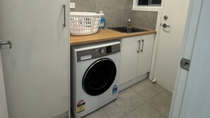 Een kleine wasruimte met een wasmachine, een droogrek en een raam boven de wasbak.