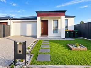 A modern two-story house with a red door, white garage doors, and a well-maintained lawn with stepping stones. - The house of joy-Glenelg Beach Gataway (Morphettville)
