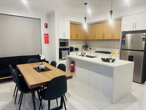 Eine moderne Küche mit weißen Schränken, einer zentralen Kochinsel und einem Essbereich mit Holztisch und schwarzen Stühlen.