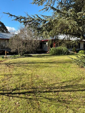 A residential property with a well-maintained lawn, a house with a red roof, and a large tree in the foreground.