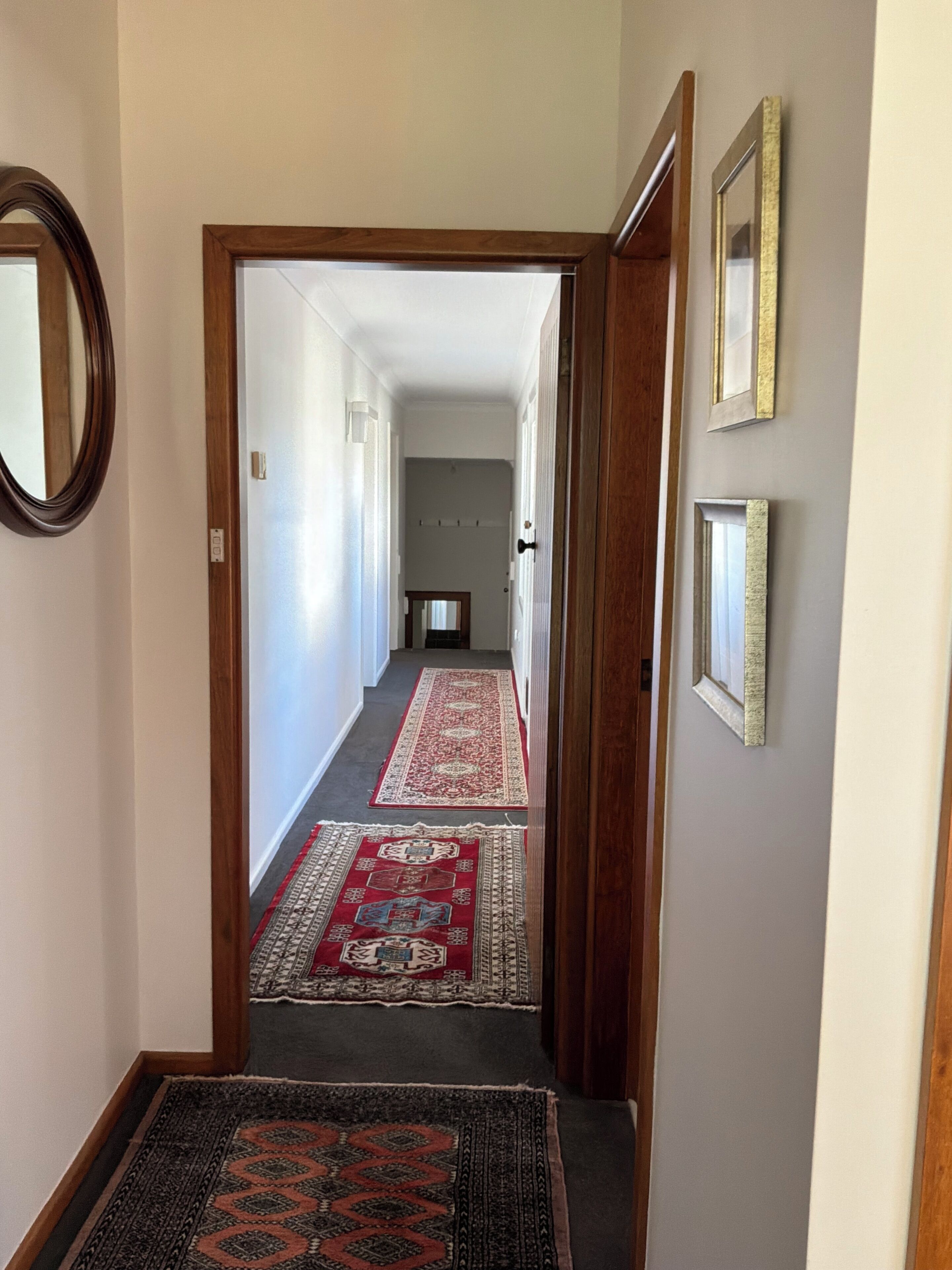 A hallway with a carpeted floor, a wooden door frame, and a mirror on the left.