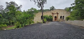 A stone building with a central entrance, surrounded by gravel and trees. - Yaupon Valley Treehouse · 2 Kings + Bunk Room · Sleeps 8 · Hill Country Canopy (West Lake Hills)